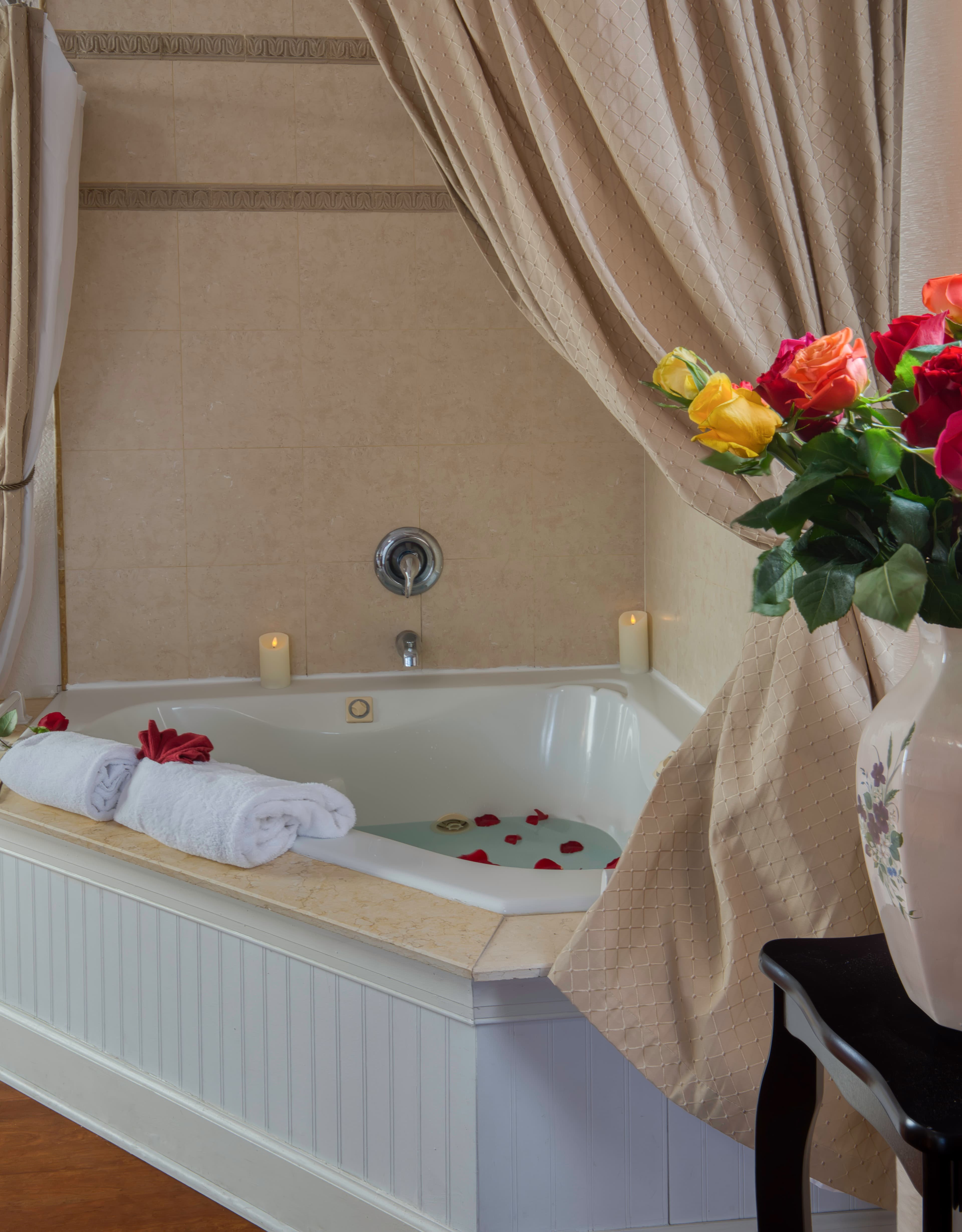 Two-person jacuzzi tub with shower, rose petals floating on water, plush white towels on tub ledge