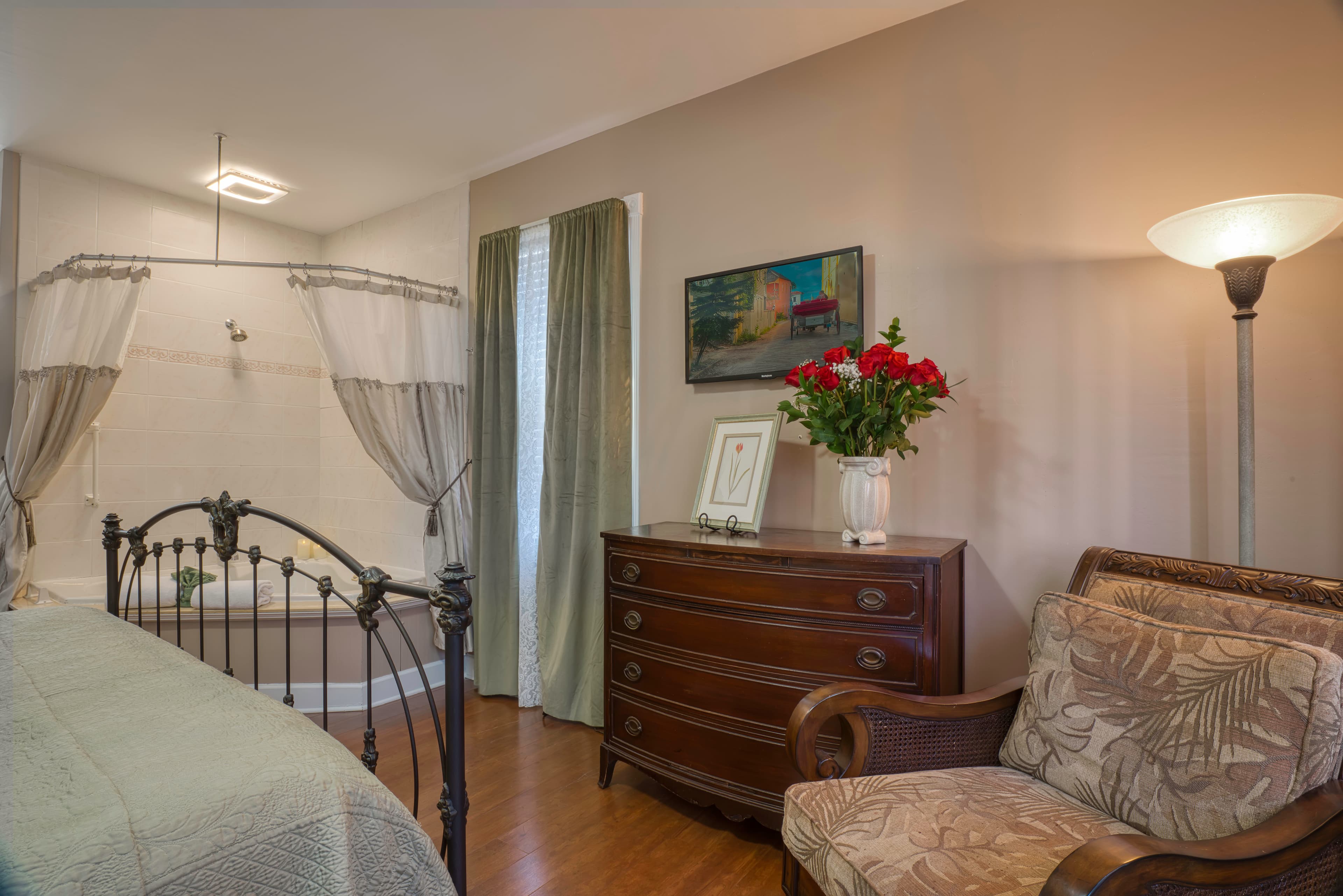 King bed, two-person jacuzzi tub with shower, comfortable armchair, dresser, and flat-screen wall-mounted TV