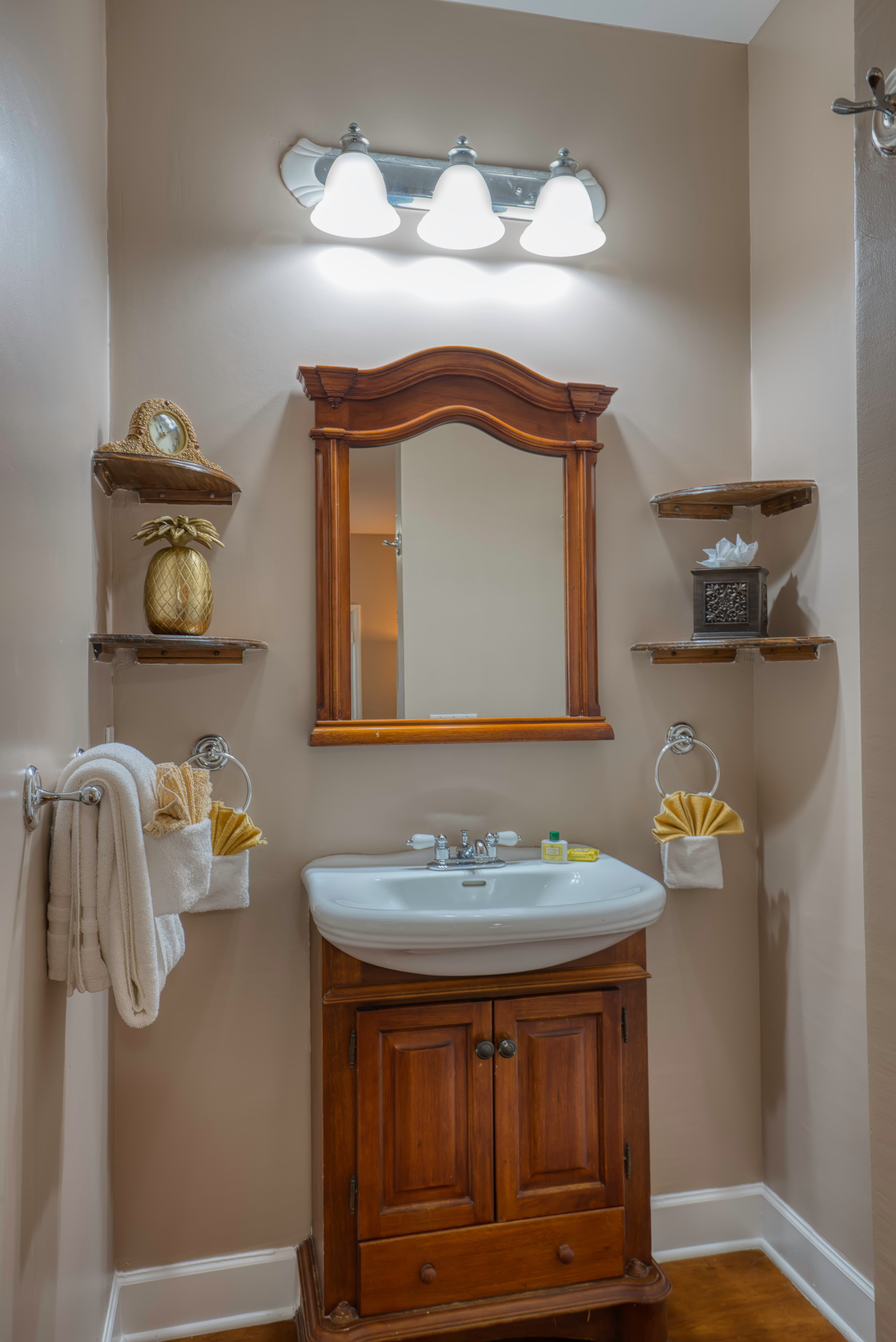 Bathroom with warm wooden vanity & white sink, coordinating wooden mirror, and plush white towels hanging nearby