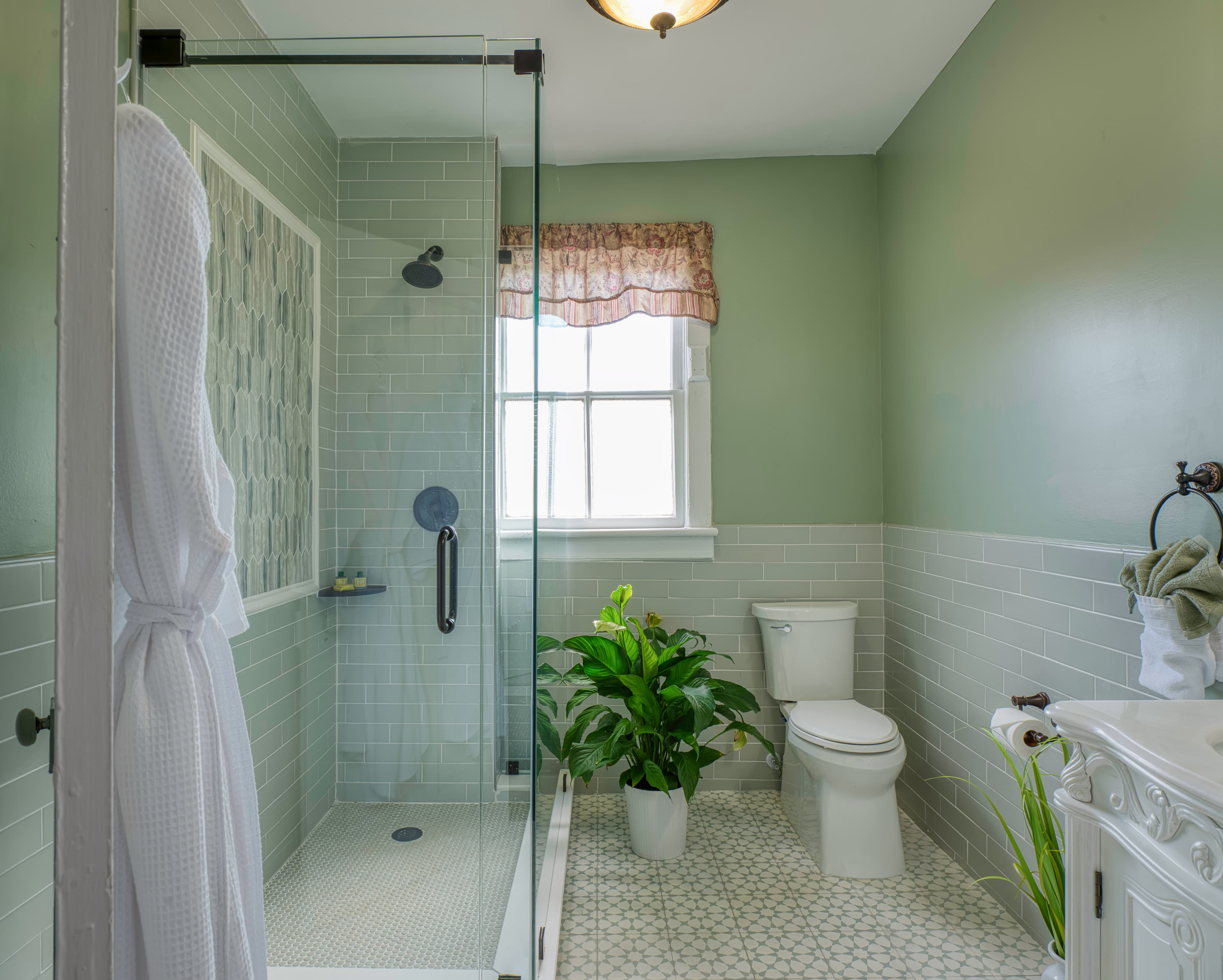 Bathroom in lovely shade of light sage green & white, white sink, toilet, and glass-enclosed shower