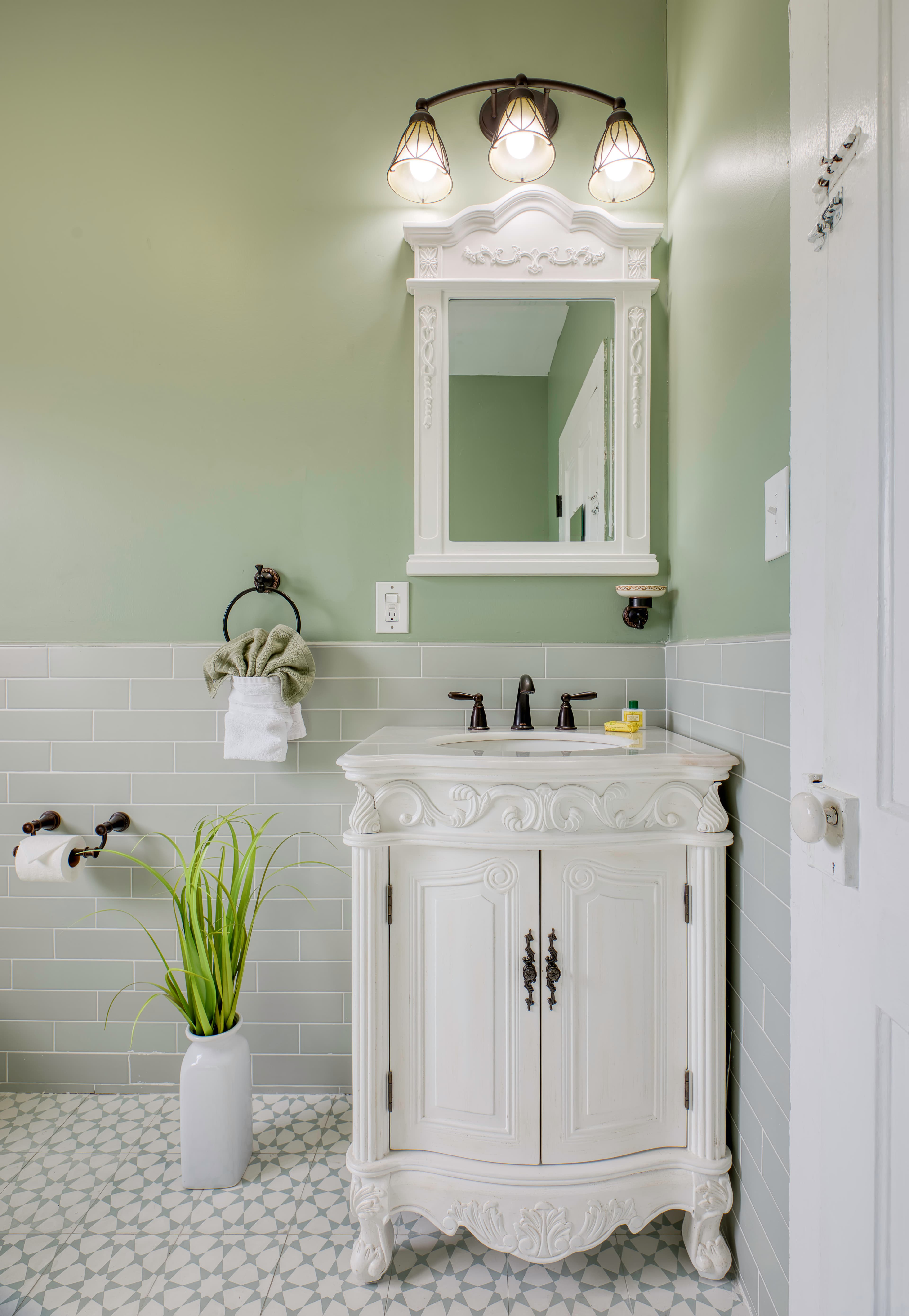 Bathroom with white wooden carved vanity & sink, coordinating mirror, and tiled floor