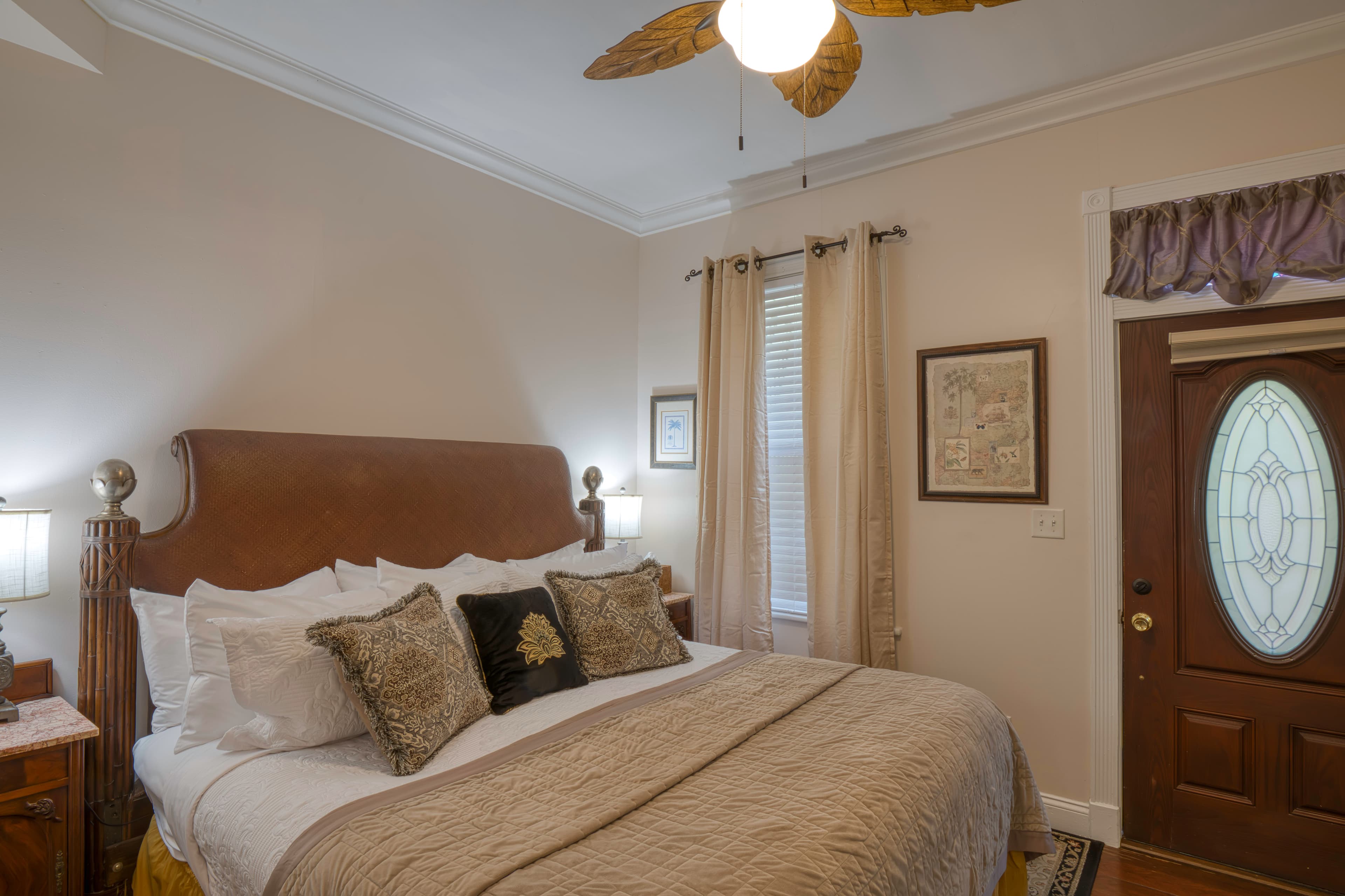 Bedroom in warm neutral shades, king bed, ceiling fan, and private entrance with beautiful wood door