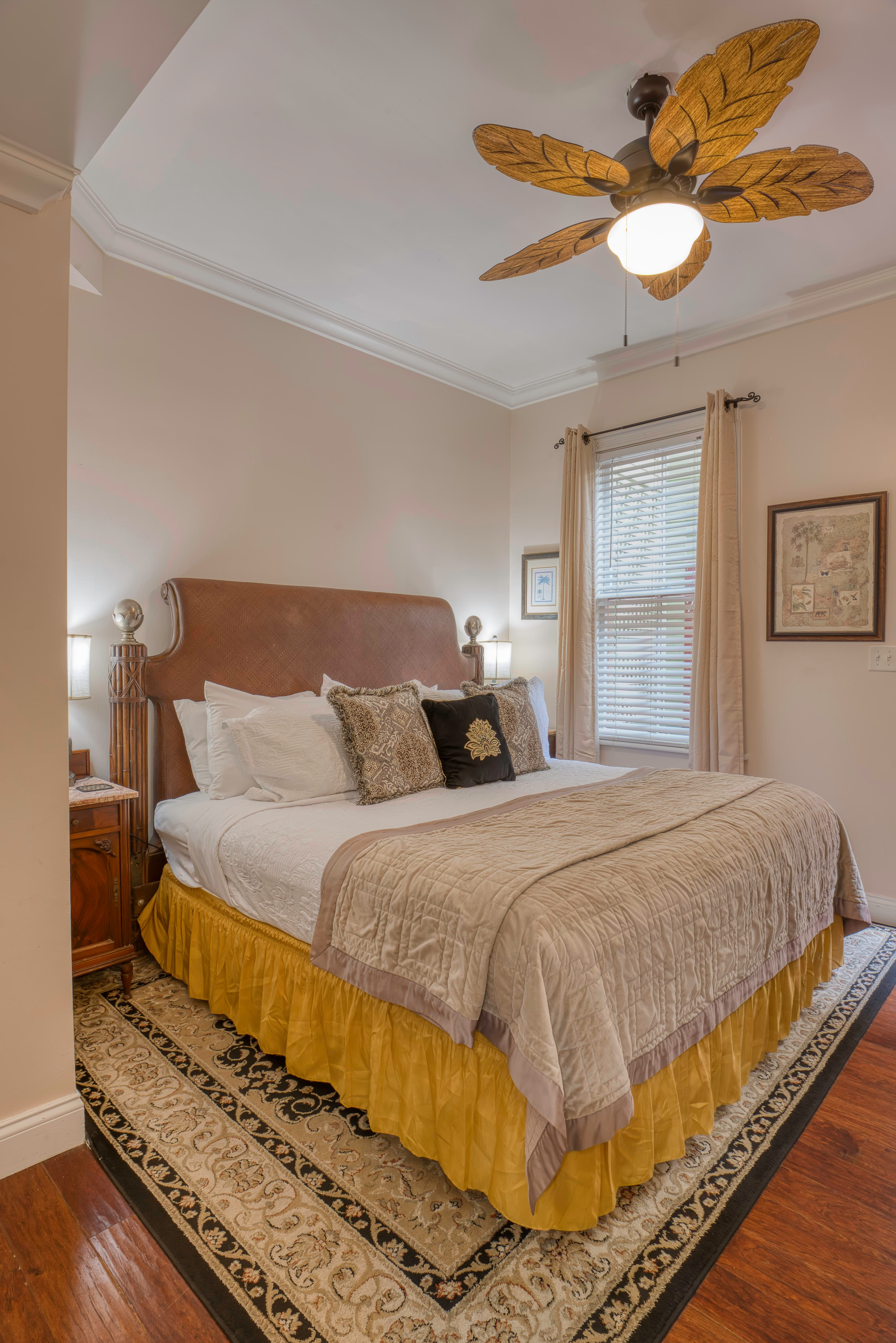Inviting bedroom in neutral shades withking bed, wood floors, oriental area rug, ceiling fan with leaf-shaped blades