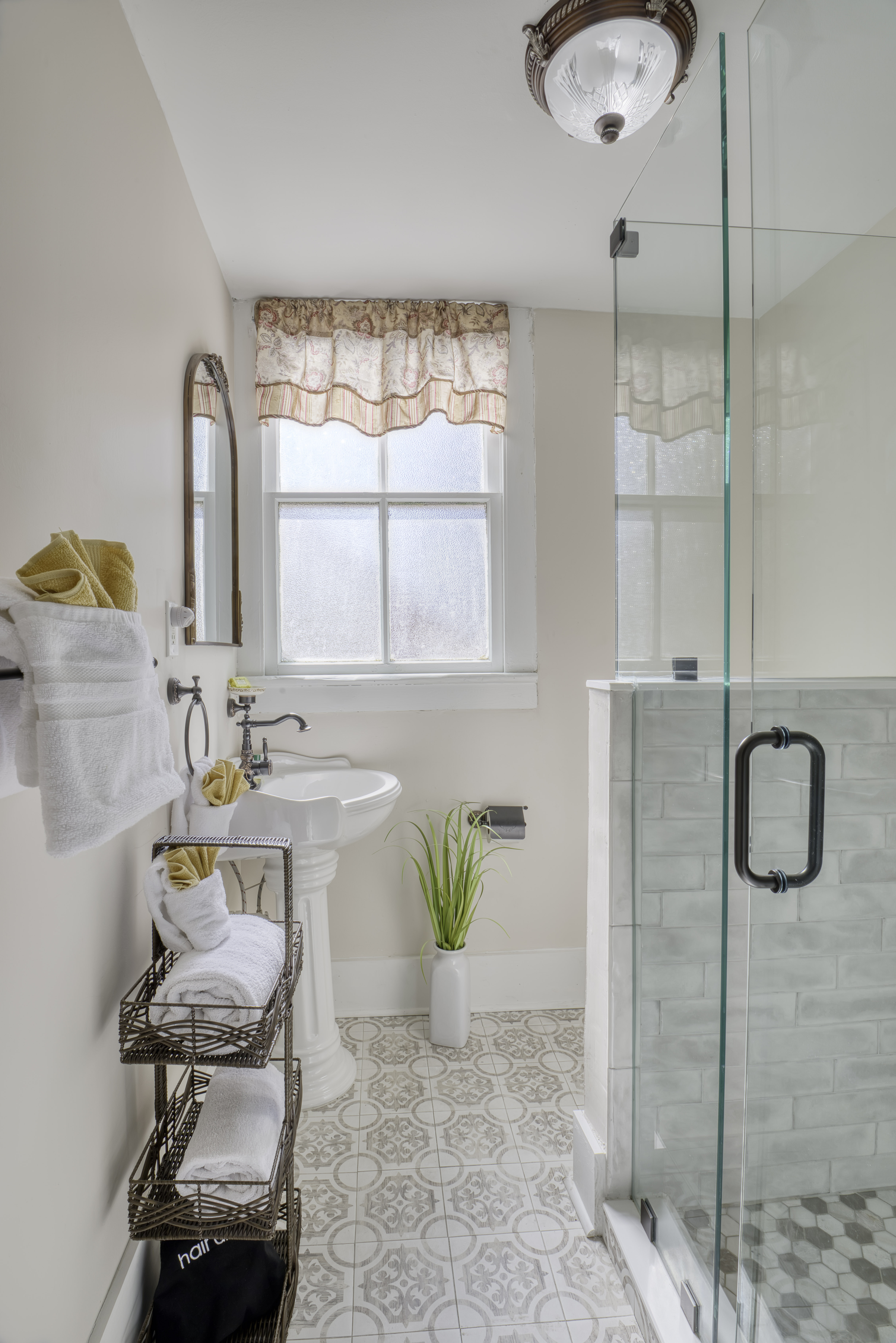 Light and airy bathroom with glass-enclosed walk-in shower, white pedestal sink, and plush white towels