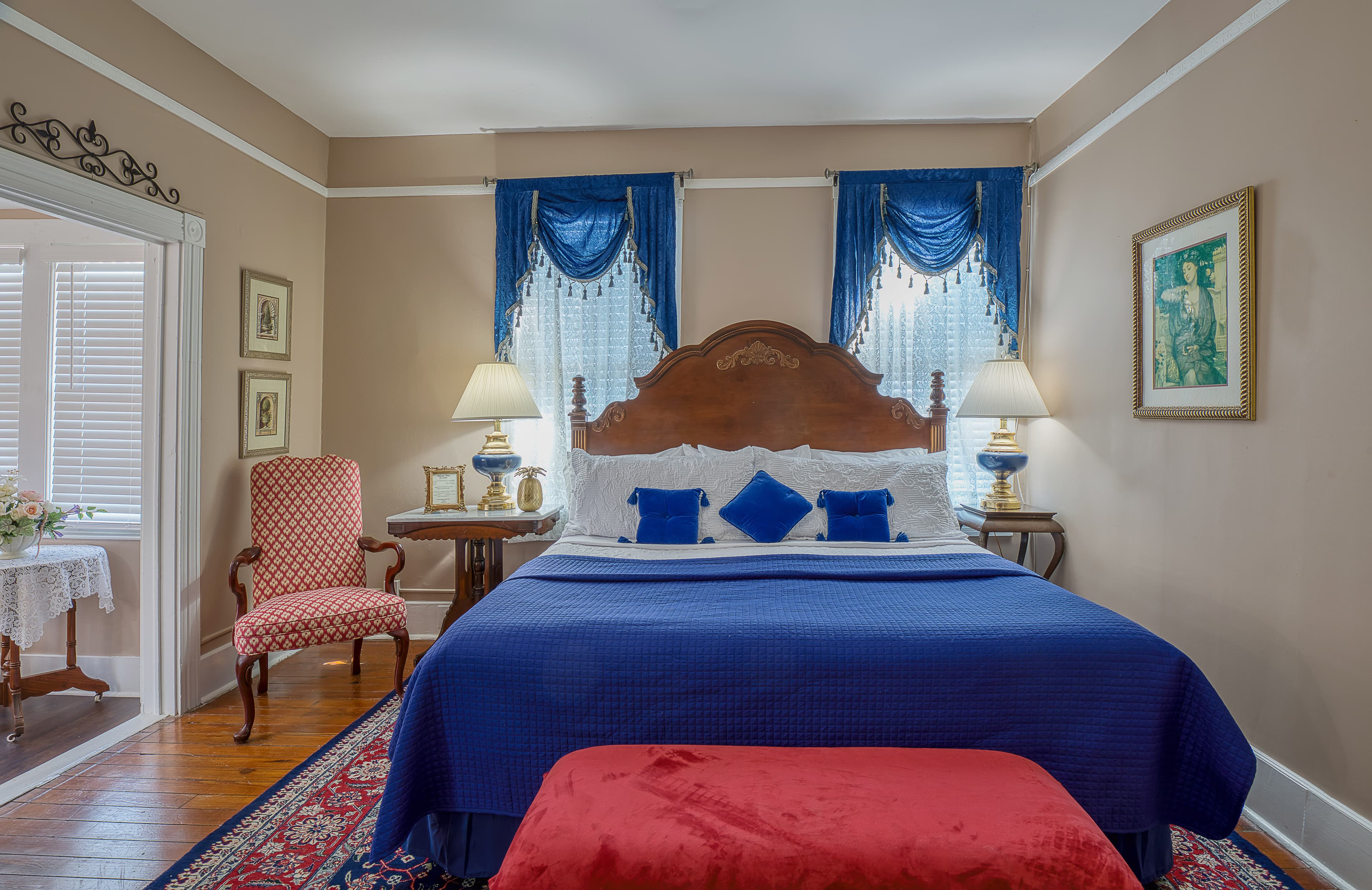 Bedroom with king bed covered in sapphire blue bedcover and pillows with matching valances on pair of windows behind