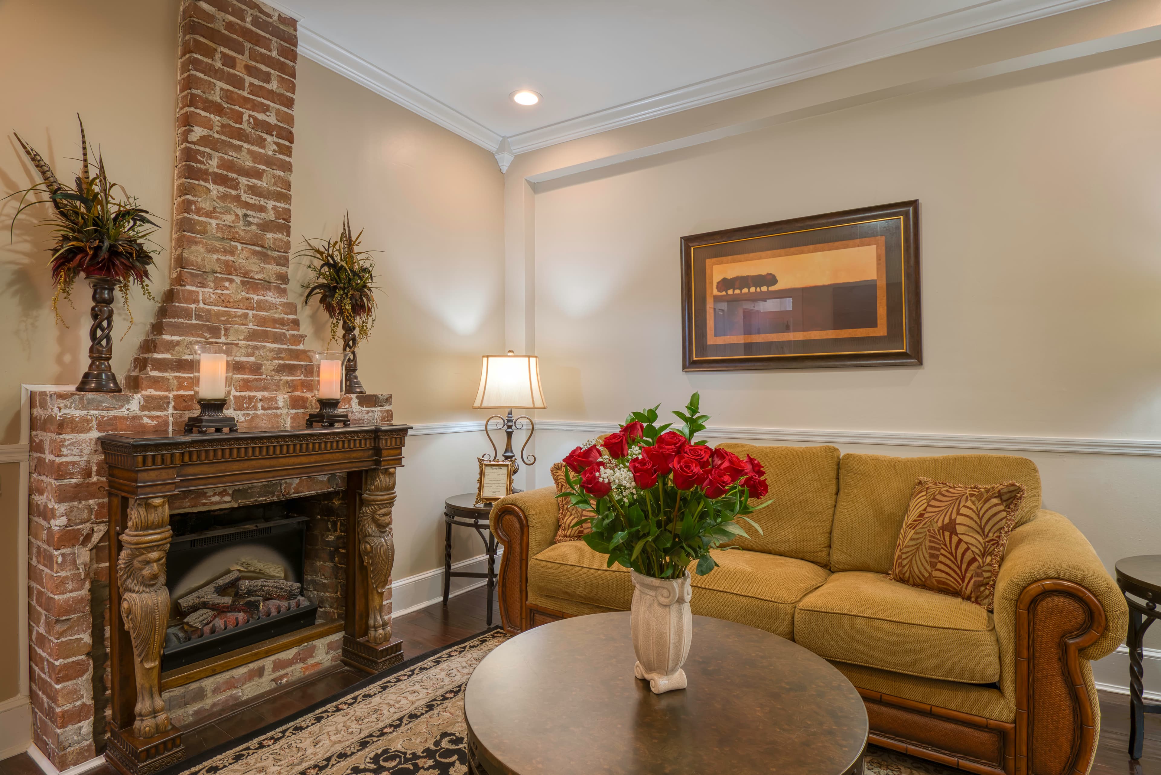 Living room with fireplace, rich gold sofa bed, round coffee table topped with vase of flowers