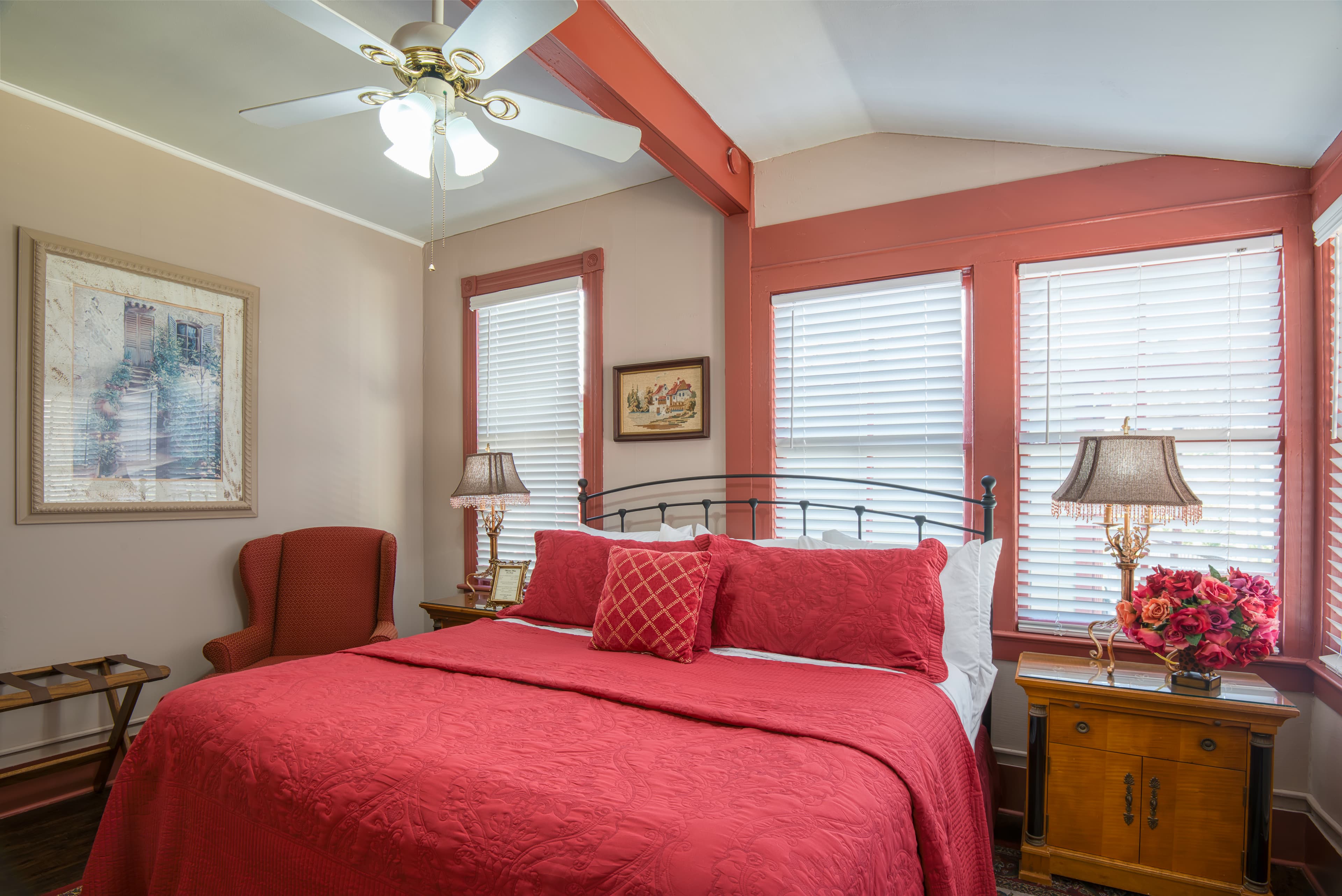 Bedroom with king bed, sun-filled windows, wooden nightstands & table lamps, ceiling fan