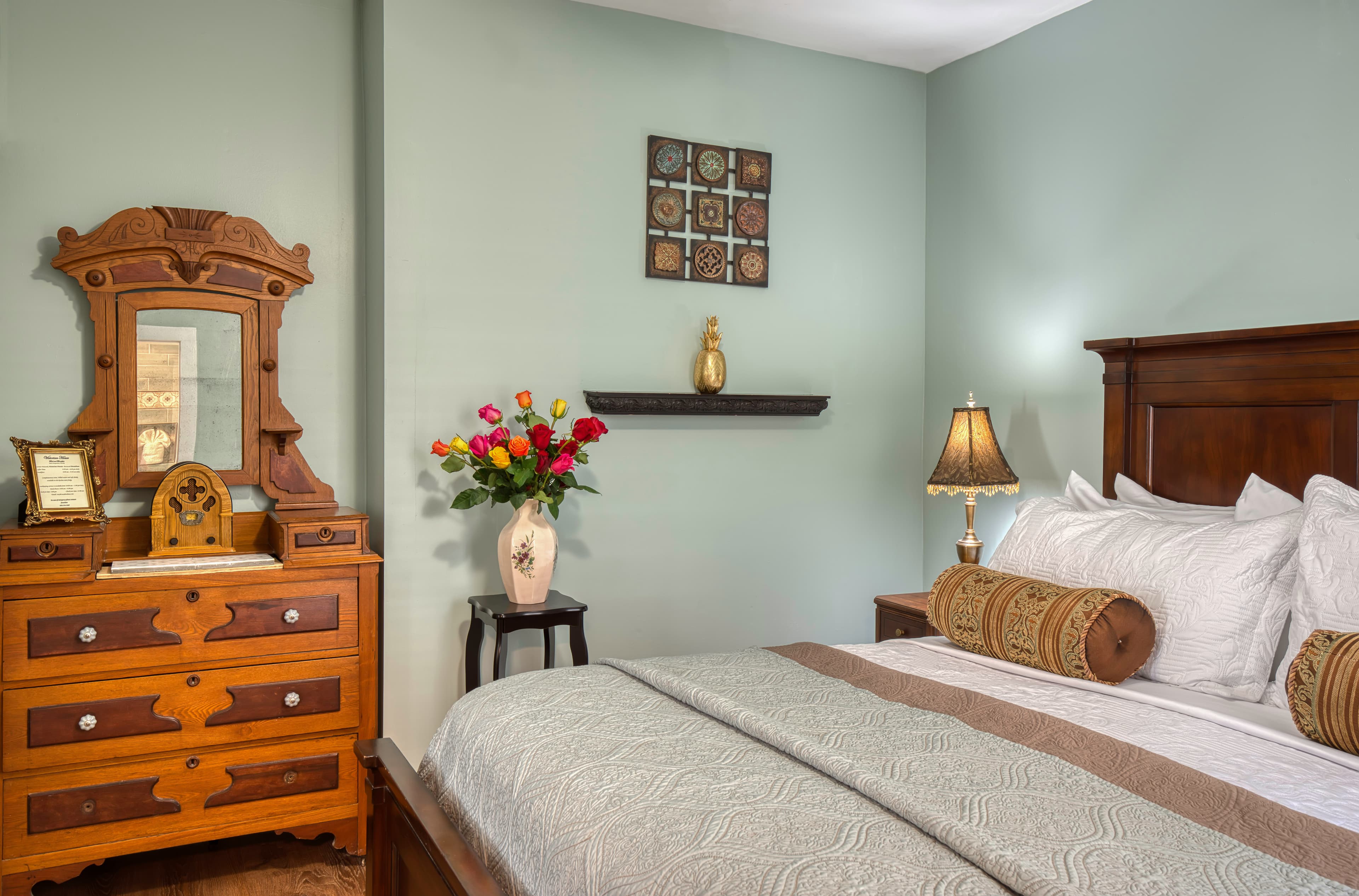 Bedroom painted in lovely light blue with king bed, dresser, and small stand with flower-filled vase