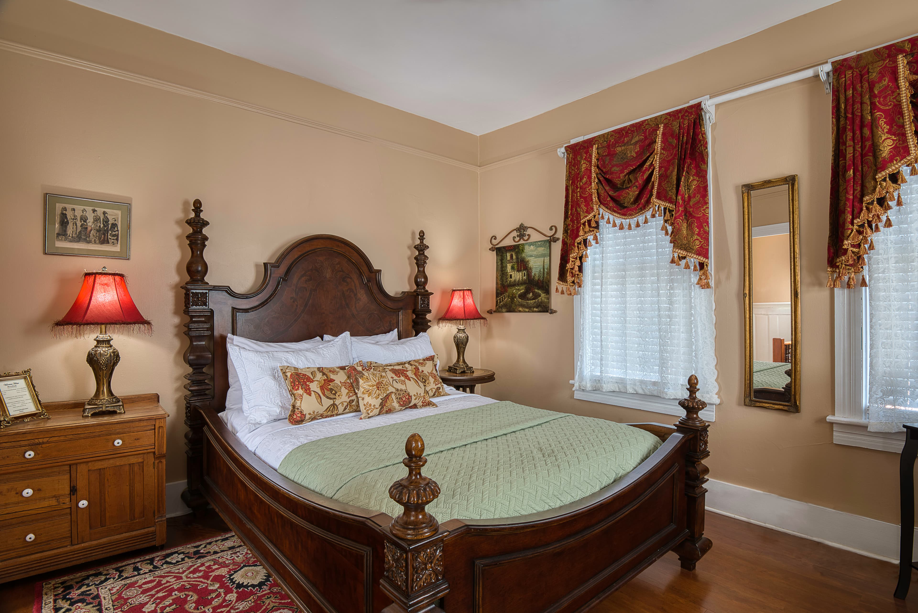 Bedroom with solid wood queen sleigh bed, wooden floors, Oriental area rug, and opulent red and gold valances