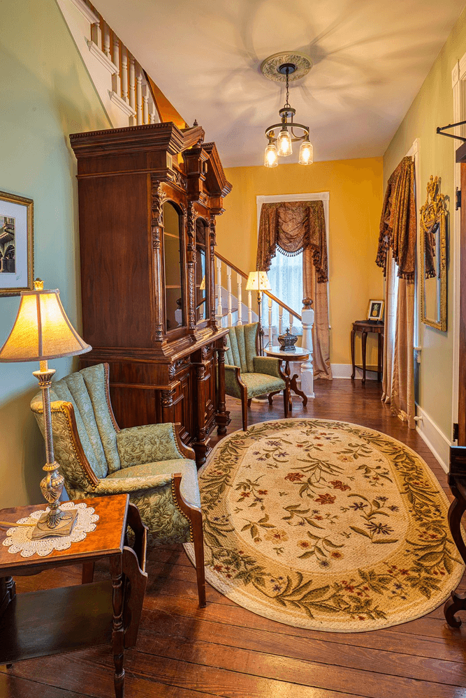 Foyer area with tall cabinet, period chairs and rug with lights and stairs in background