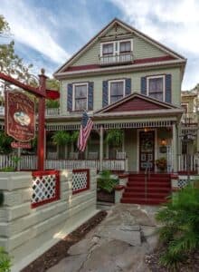 A charming green and red house with a porch, featuring an American flag and a sign for a bed and breakfast. A charming green and red house with a porch, featuring an American flag and a sign for a bed and breakfast.