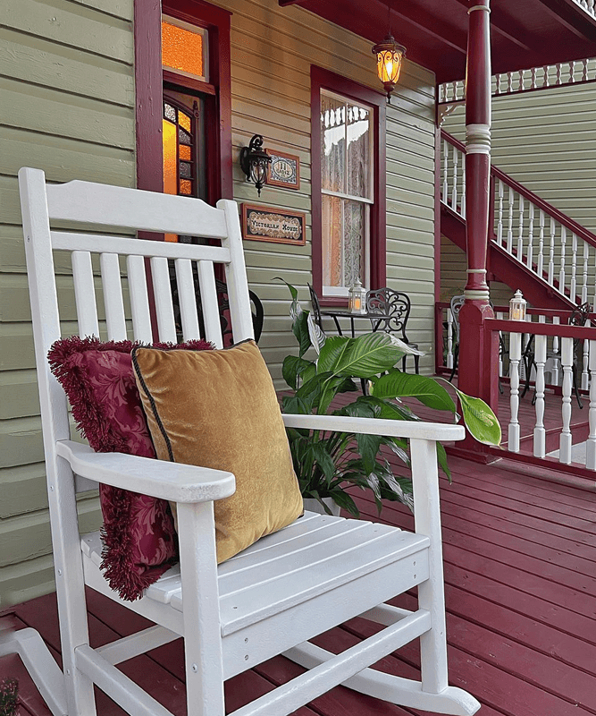 White rocker on front porch by front door with victorian house sign