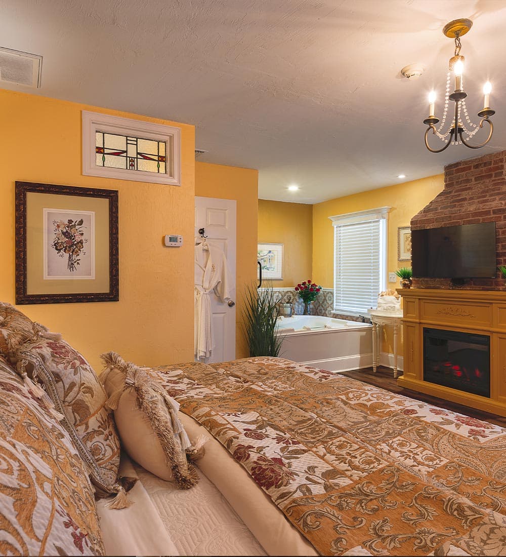 A cozy bedroom with a yellow theme, featuring a large bed, a fireplace, and a modern bathtub.