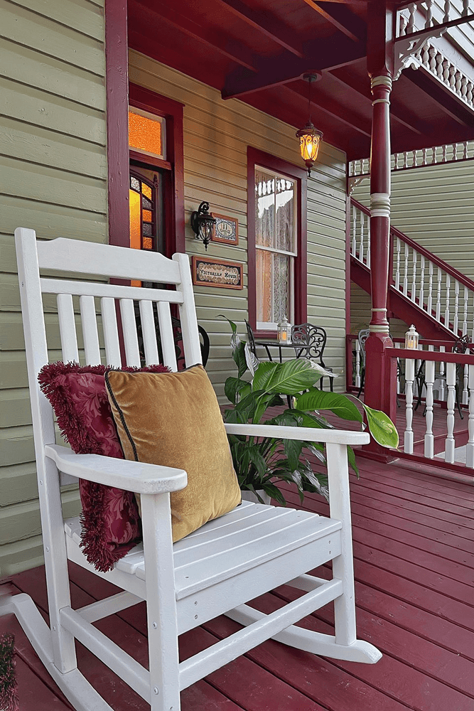 White rocker on front porch by front door with victorian house sign
