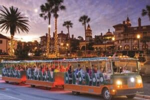 A brightly lit tram carries passengers through a festive scene with palm trees and historic buildings at sunset. A brightly lit tram carries passengers through a festive scene with palm trees and historic buildings at sunset.