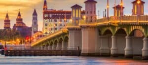 A historic bridge illuminated at sunset, with buildings in the background reflecting on the water. A historic bridge illuminated at sunset, with buildings in the background reflecting on the water.