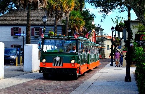 A green and orange trolley on a brick street lined with palm trees