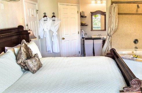 Bedroom with sleigh bed, white robes hanging, sink and corner jacuzzi tub