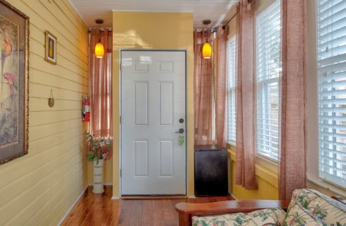 Breezeway with yellow walls, sitting chair, large windows and white door leading to a bedroom