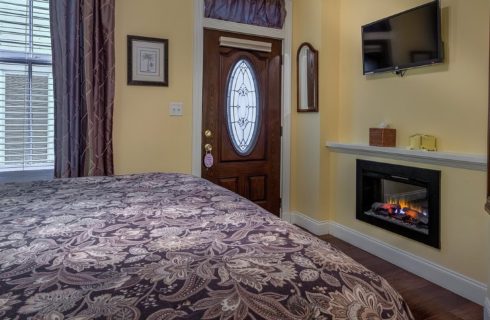 Bed with floral quilt in guestroom with yellow walls, gas fireplace and TV hung overhead