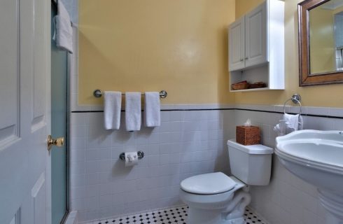 Bathroom with yellow walls and white tile with toilet, cabinet, pedestal sink and mirror