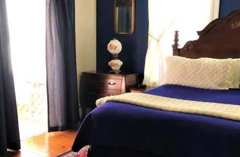 Bed with antique wood headboard in guest room with navy walls, bright windows and patio door