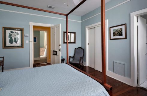 Guestroom with four poster bed, light blue walls and doorway into bathroom