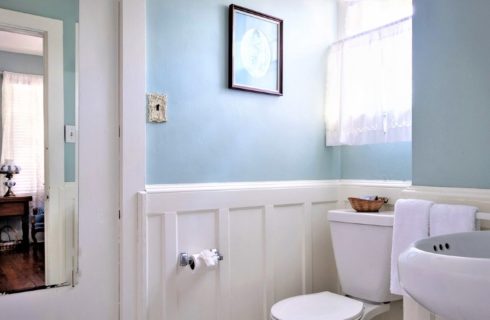 Bright bathroom with window, pedestal sink, light blue walls with wainscoting trim