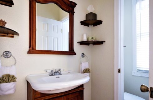 Single sink vanity with mirror and hanging shelves next to doorway to private toilet closet