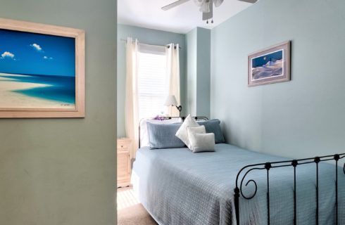 Small guest room with light blue walls and twin bed in front of a bright window