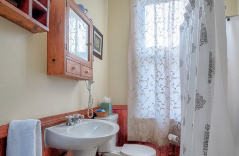 Bathroom with large window, white pedestal sink and wooden wainscoting trim