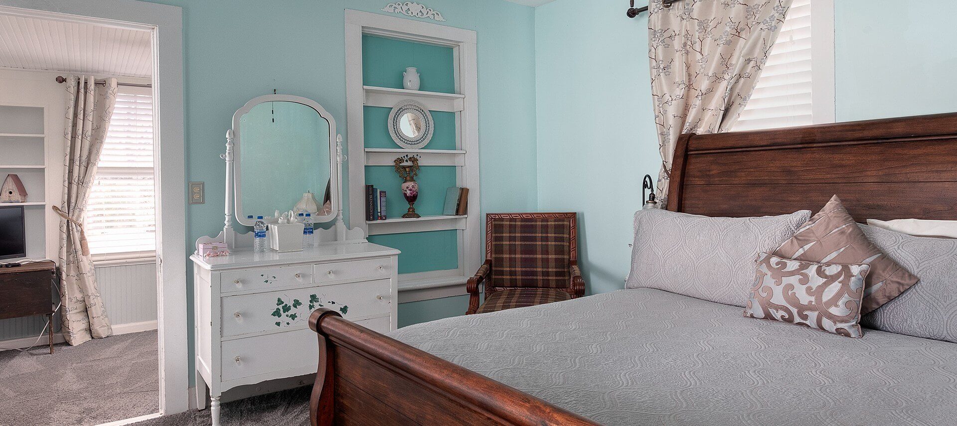 Guestroom with sleigh bed, white dresser with mirror, and doorway into sitting room