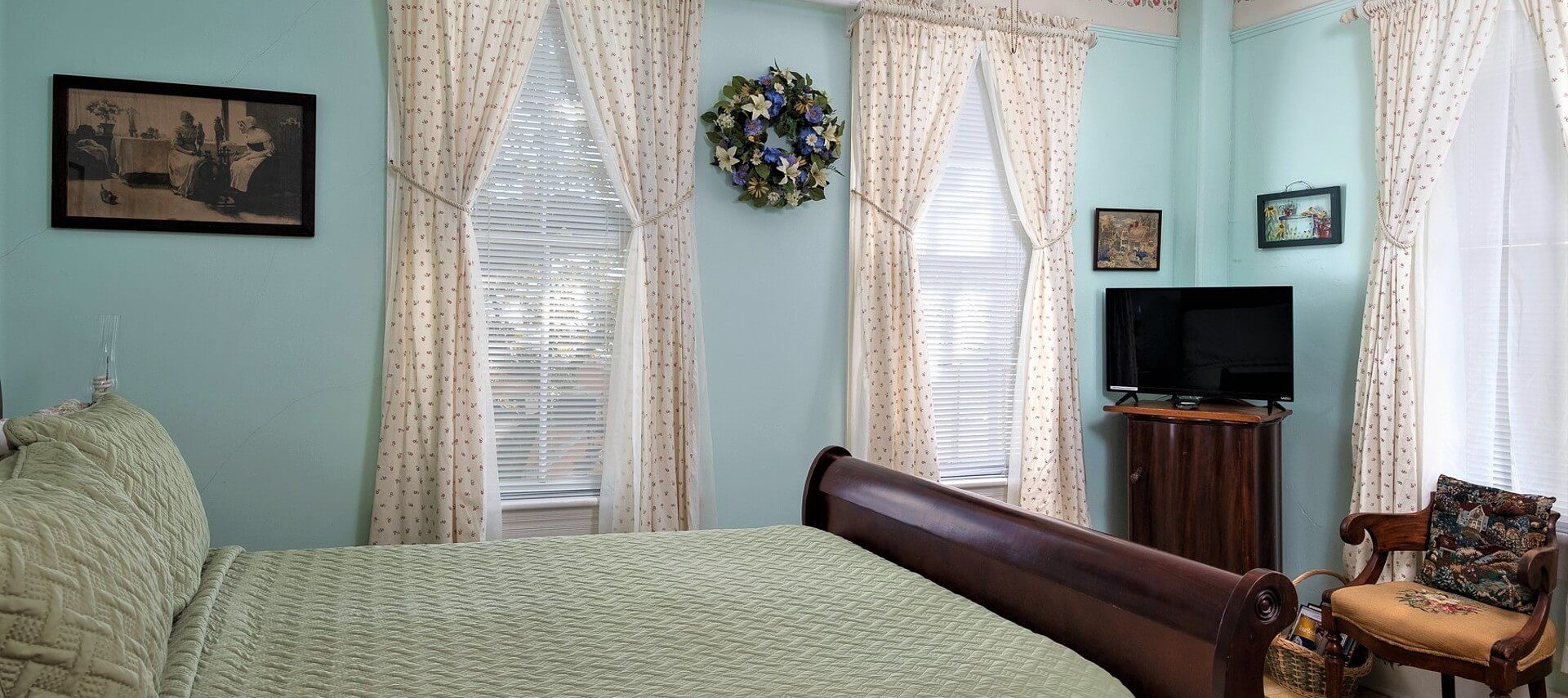 Guestroom with sleigh bed, large windows with floral curtains and sitting chair