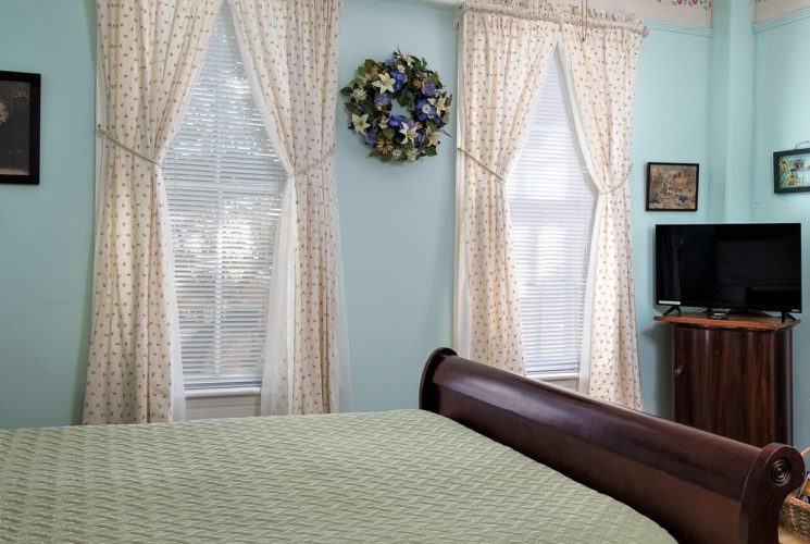 Guestroom with sleigh bed, large windows with floral curtains and sitting chair