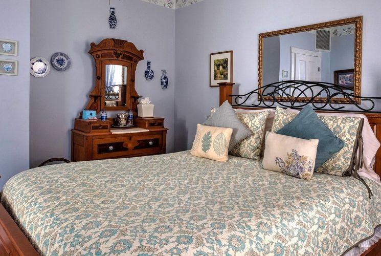 Bed with floral quilt and wood and iron headboard in room with decorative dresser and large framed mirror